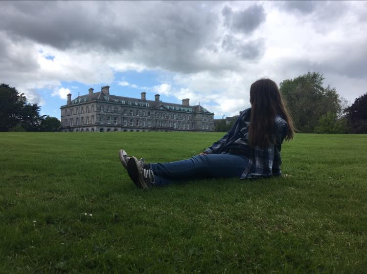 girl sits on grass and and admires big manor house
