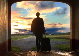 Person stands with luggage in front of a sunset
