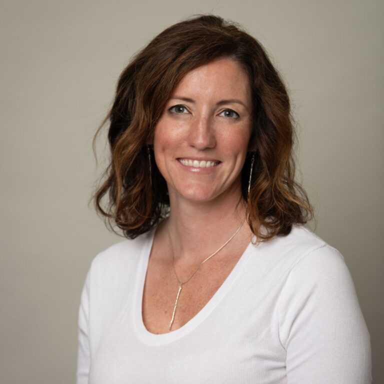 Learn director cara simon poses for a professional headshot wearing a brown jacket.