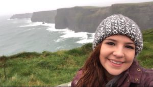 student talking a selfie at the cliffs of Moher with waves crashing off the coastline