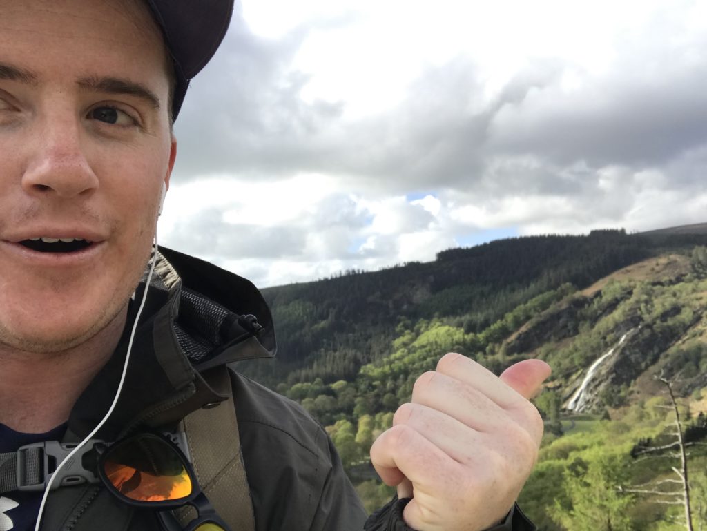 Hiker points over his shoulder to a waterfall in the distance