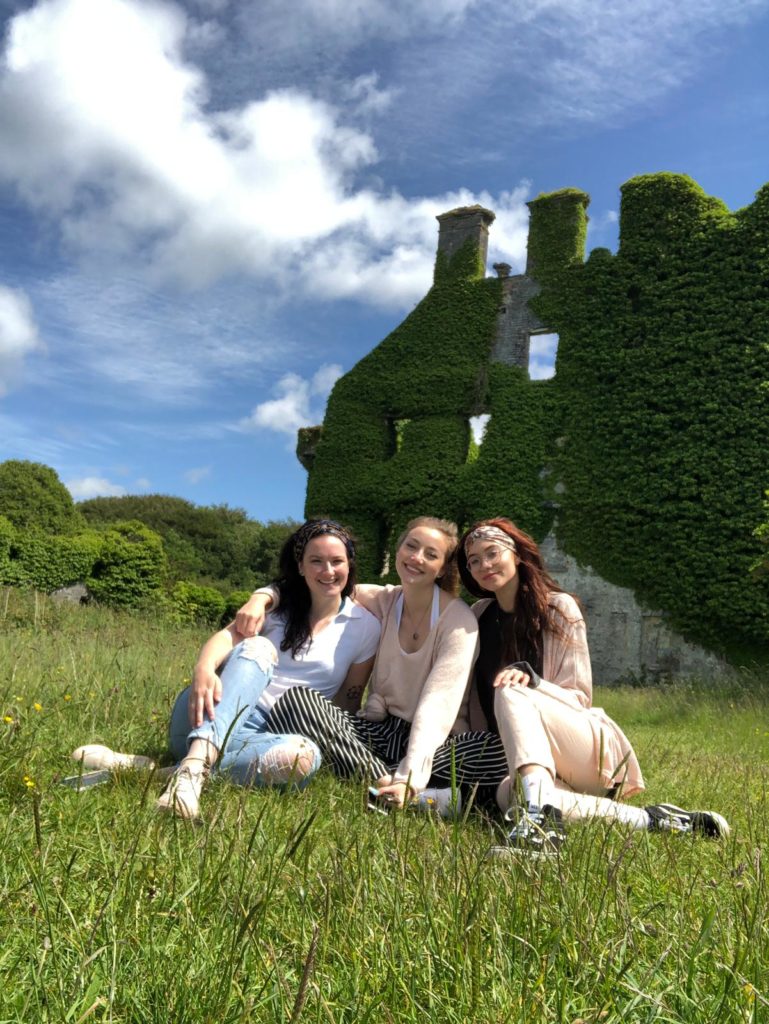 Three students sit together in the grass in front of Menlo castle