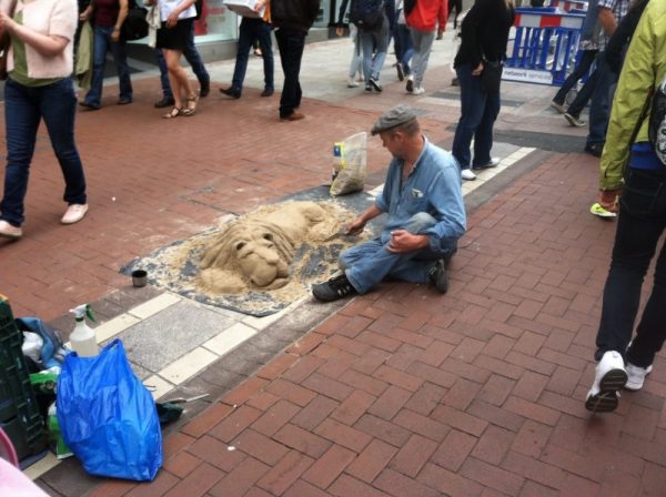 A street artist in Dublin sculpts a dog out of sand